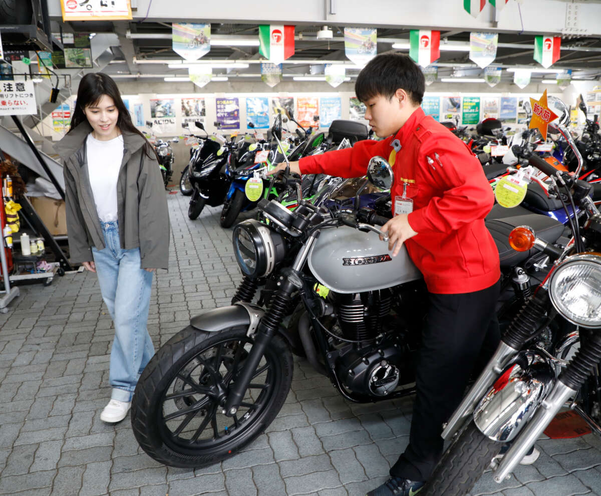 たくさんのバイクが並ぶレッドバロン店内でスタッフからバイクを見せてもらっている女性客