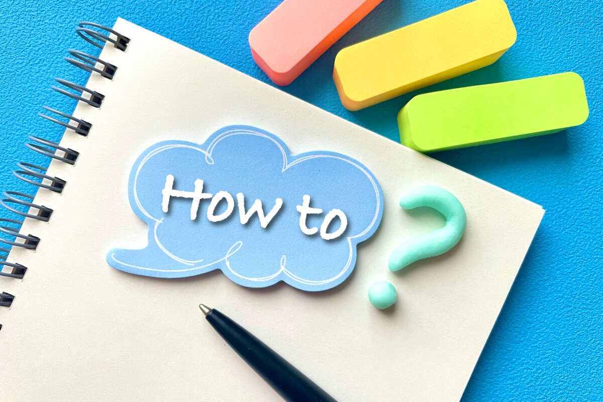 「How to」と書かれた吹き出しとノート、ペン、付箋が置かれている