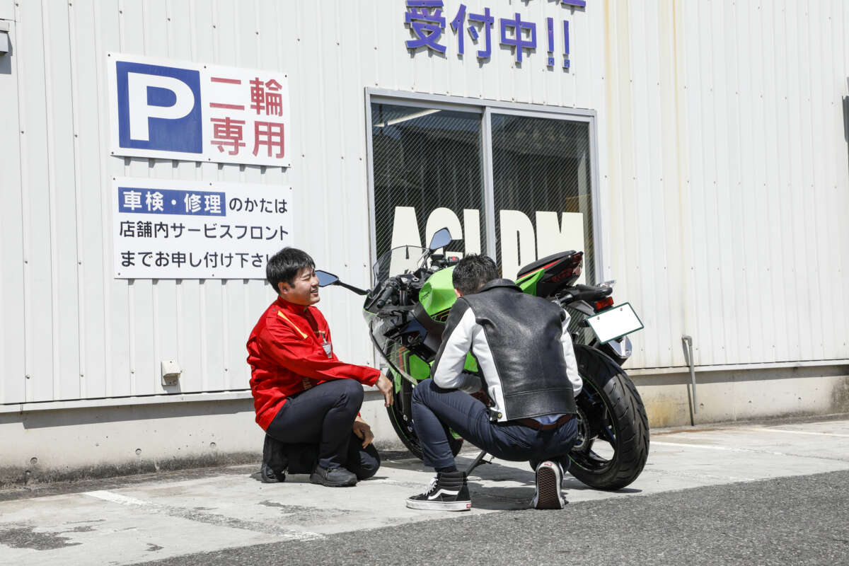 レッドバロンの舗前でバイクの横にしゃがんで談笑するスタッフと男性