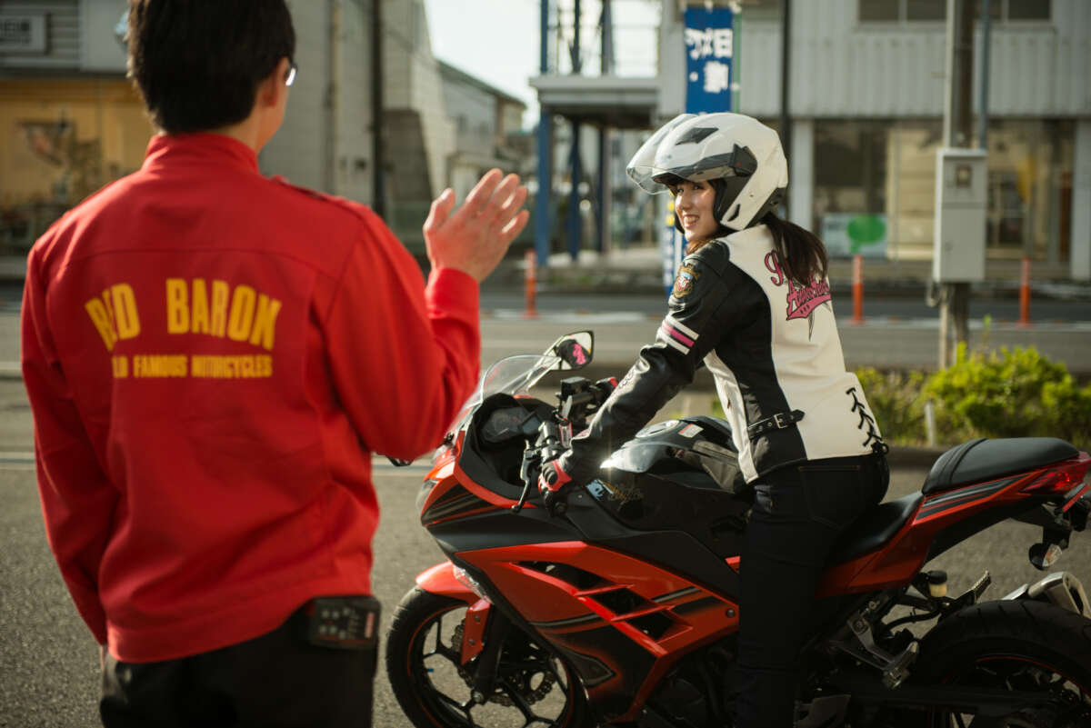バイクにまたがる女性を見送るレッドバロンの従業員