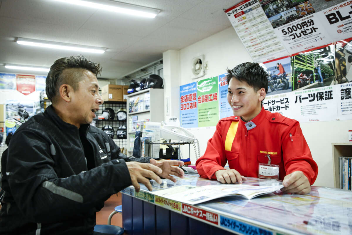 店舗のカウンターで書類を見ながら男性客と談笑するレッドバロンのスタッフ