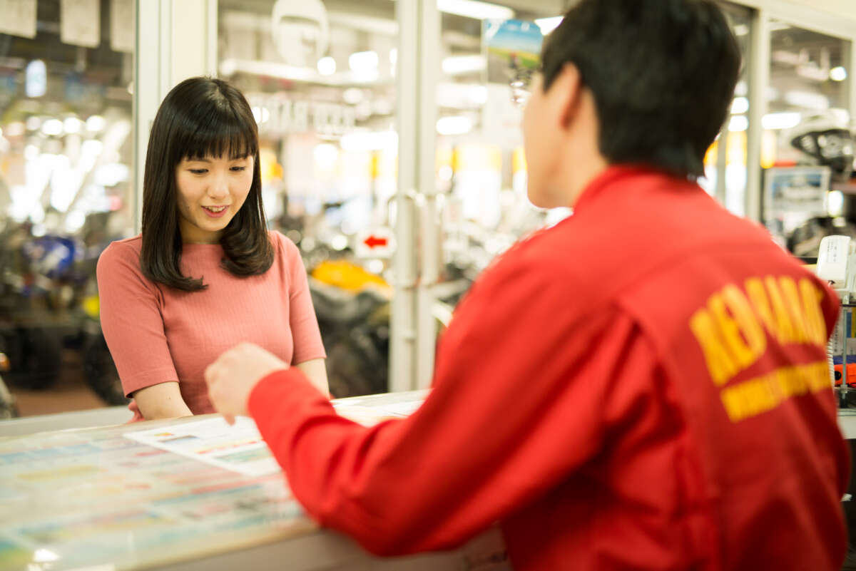 レッドバロン店内のカウンターでスタッフの説明を聞く女性