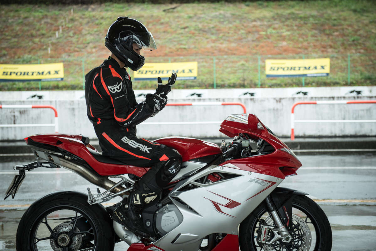 レーシングスーツ姿のライダーがサーキットでスーパースポーツバイクにまたがる様子