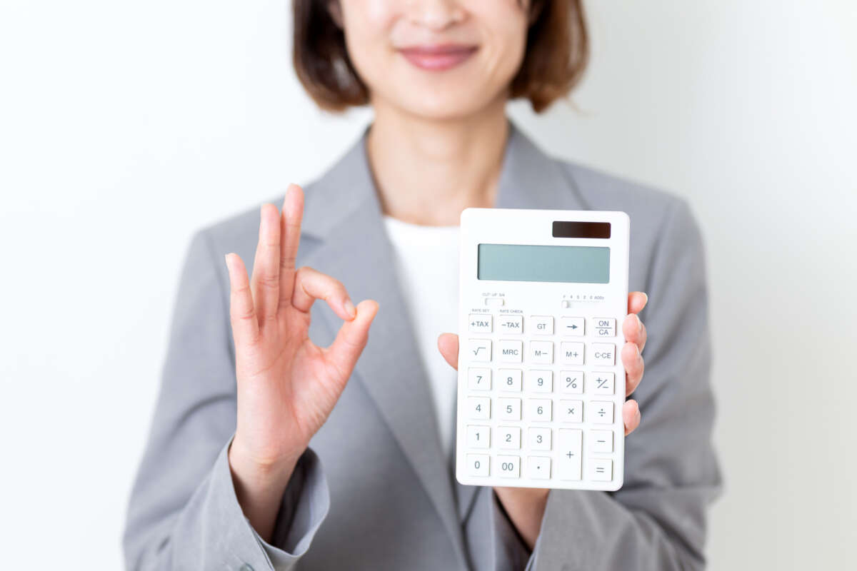 白い電卓を持って丸サインをするスーツ姿の女性