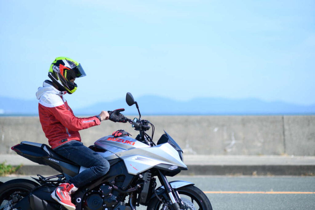 ヘルメットを着用したライダーが海沿いの道路でバイクに乗る様子