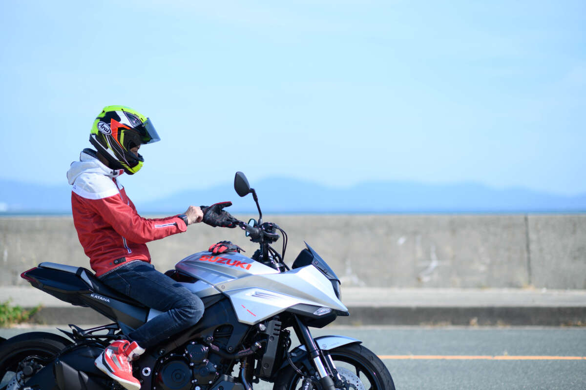 ヘルメットを着用したライダーが海沿いの道路でバイクに乗る様子