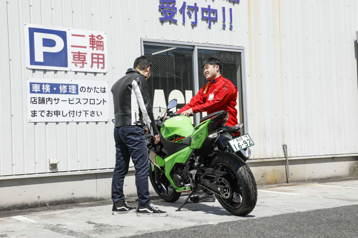 レッドバロン店舗前でスタッフと来店客がバイクを確認している様子