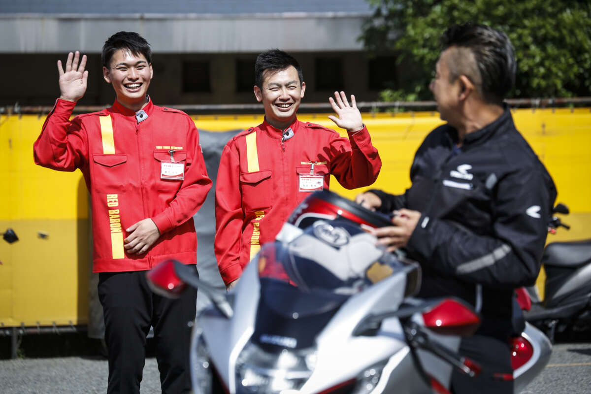 バイクにまたがる男性を見送るレッドバロンのスタッフたち