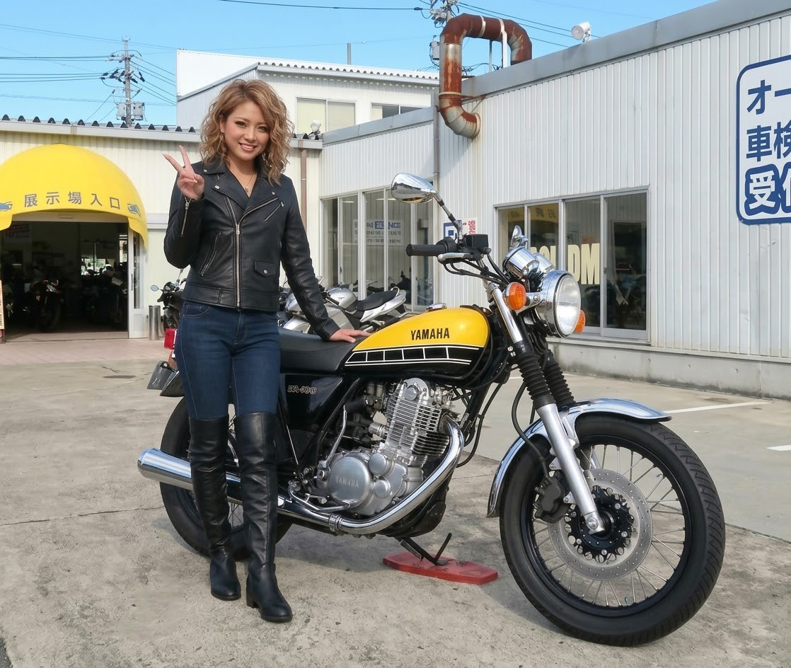 バイクの横に立ちピースをする女性ライダー