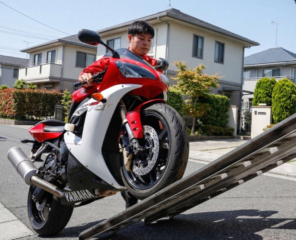 バイクをスロープに押し上げているレッドバロンのスタッフ
