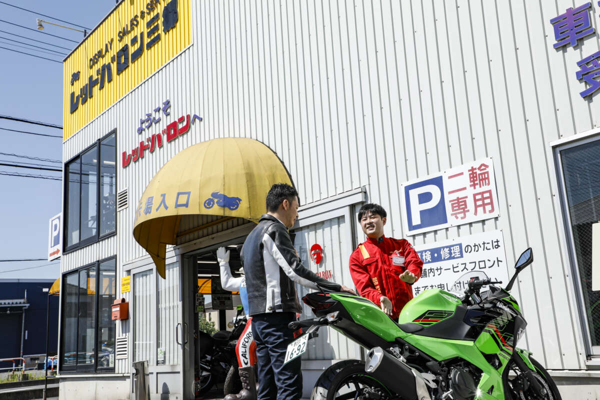 レッドバロンの店舗前でバイクを挟んで談笑するスタッフと男性