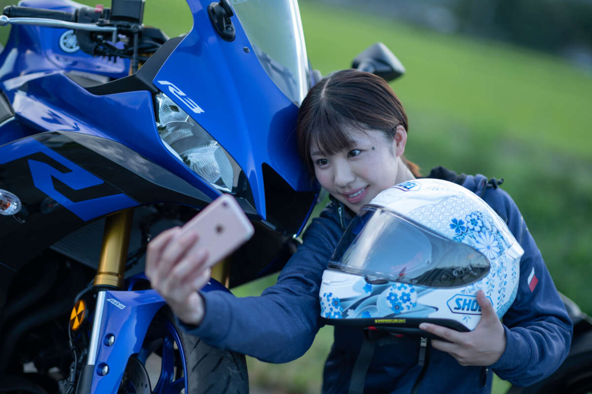 バイクに寄り添い、ヘルメットを持ってスマートフォンで自撮りをする女性