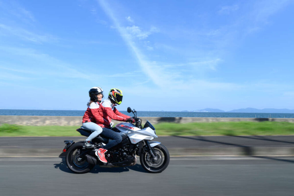 青い空と海を背景に、海沿いの道を2人乗りで走るバイク