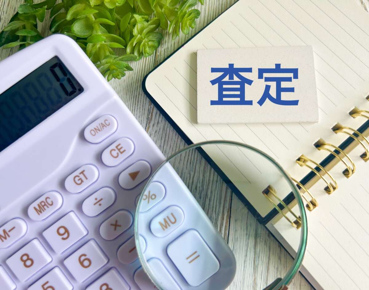 電卓と虫眼鏡、「査定」と書かれたカードが置かれたノート