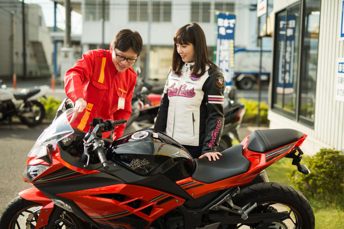 赤と黒のバイクの前で、レッドバロンのスタッフから説明を受ける女性