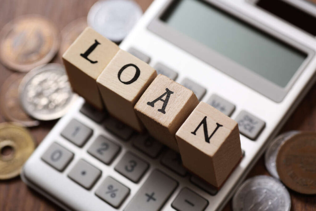 電卓の上に置かれた「LOAN」と書かれた木製ブロックと、周囲に散らばる硬貨